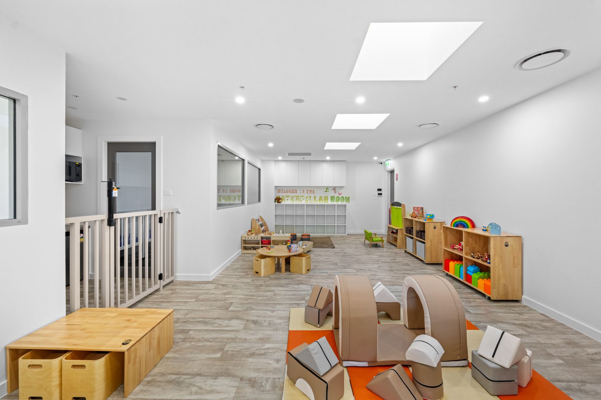 Interior of a well-lit daycare room. Features include wooden shelves, toy blocks, and a play fort.