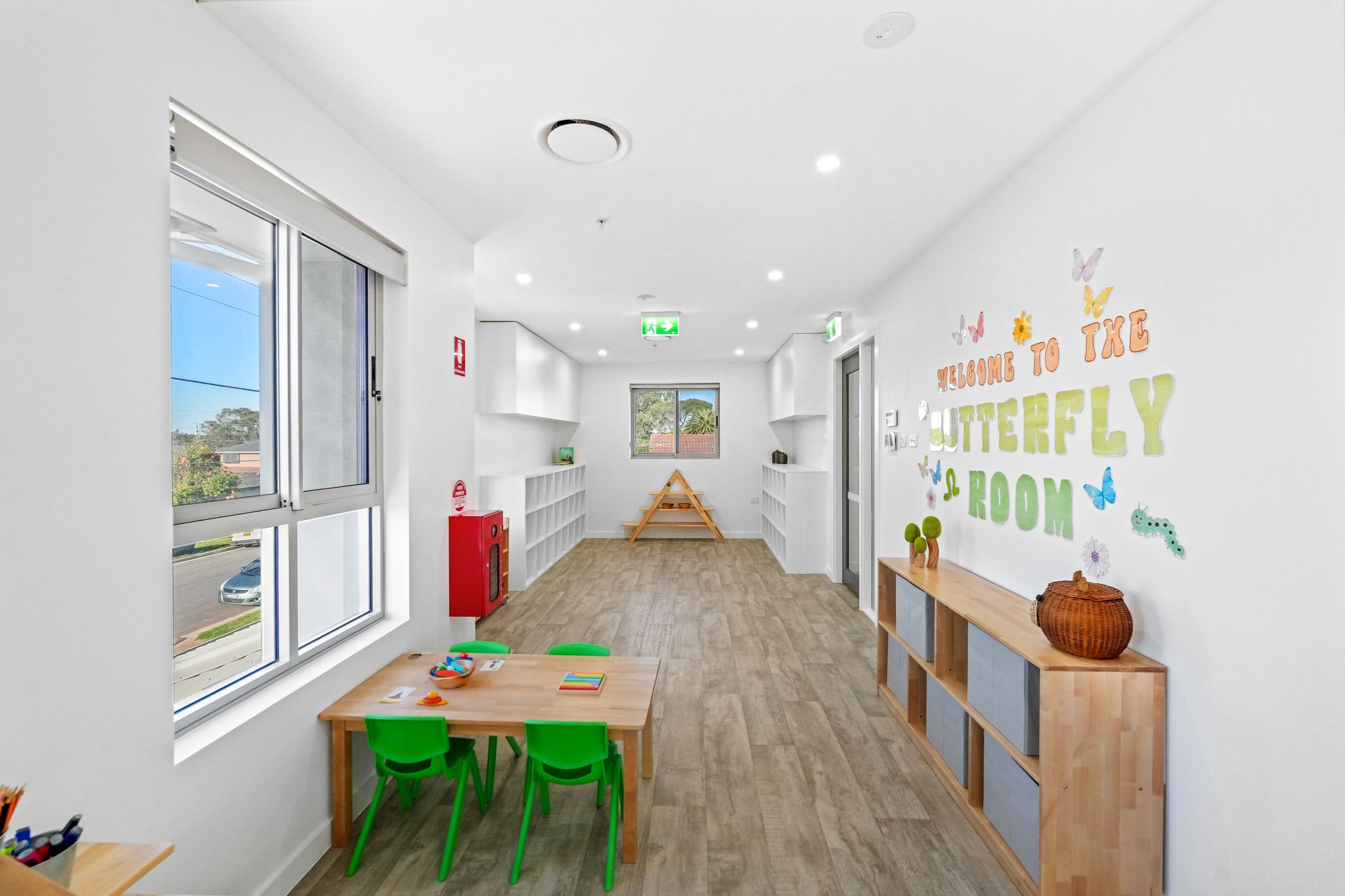 Long hallway in a brightly lit children's center, with a table, storage, and a sign 