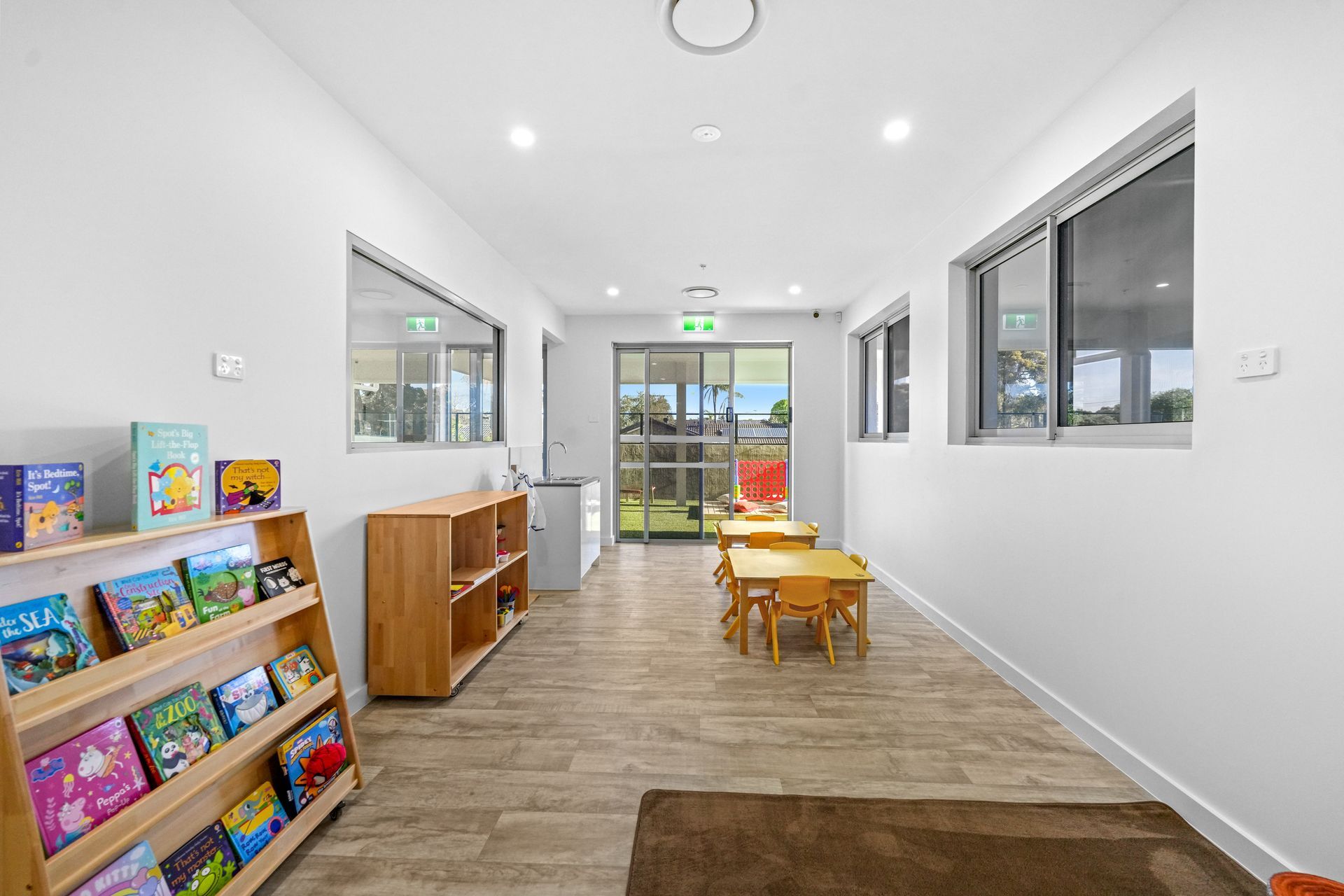 Childcare room with bookshelves, small tables, and windows.