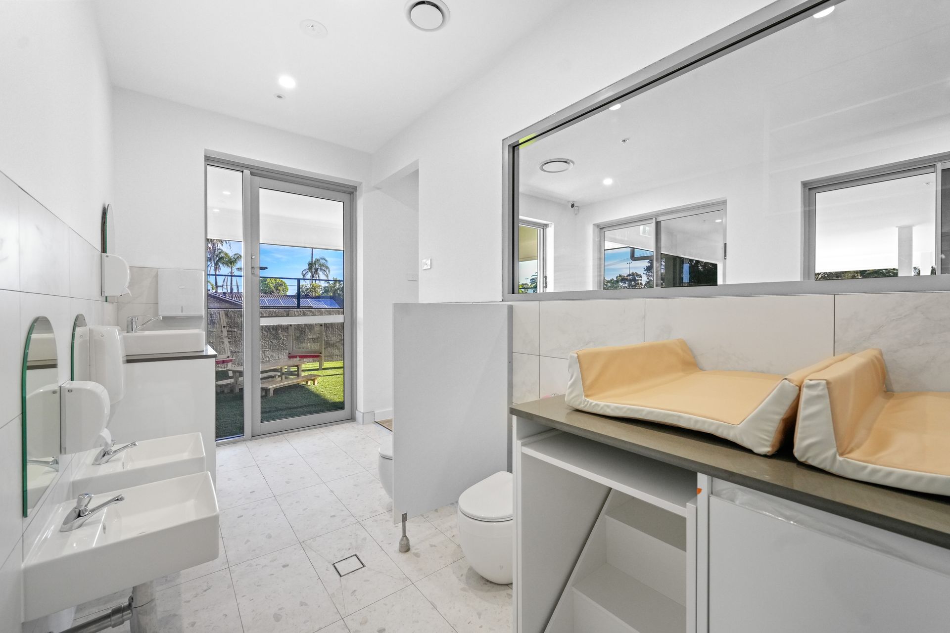 Brightly lit, modern Children nappy change room with sinks, changing stations, and a toilet.