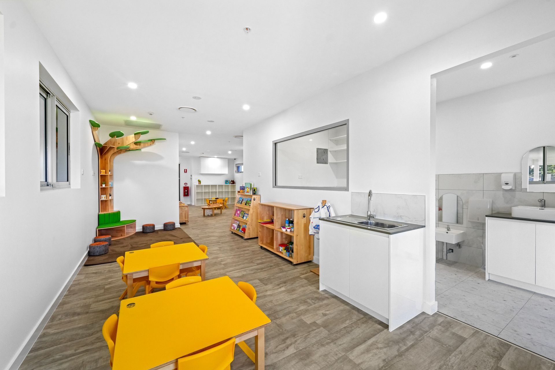 Bright preschool classroom with yellow tables, a tree structure, and a craft sink area.