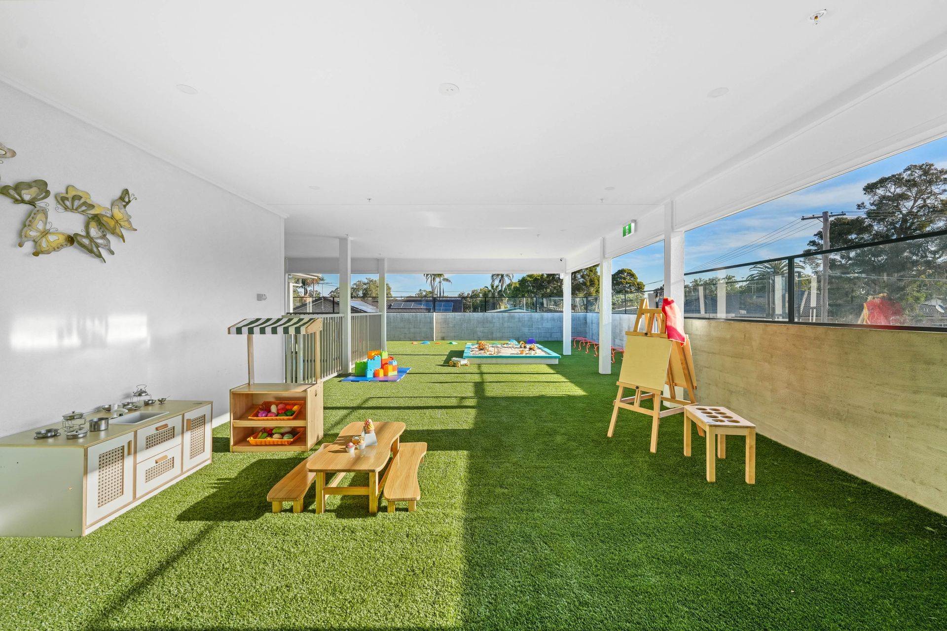 Outdoor daycare play area with artificial turf, picnic table, and art easel.
