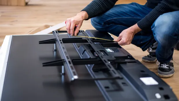 Person installing a TV mount on a flat-screen TV, indoors.