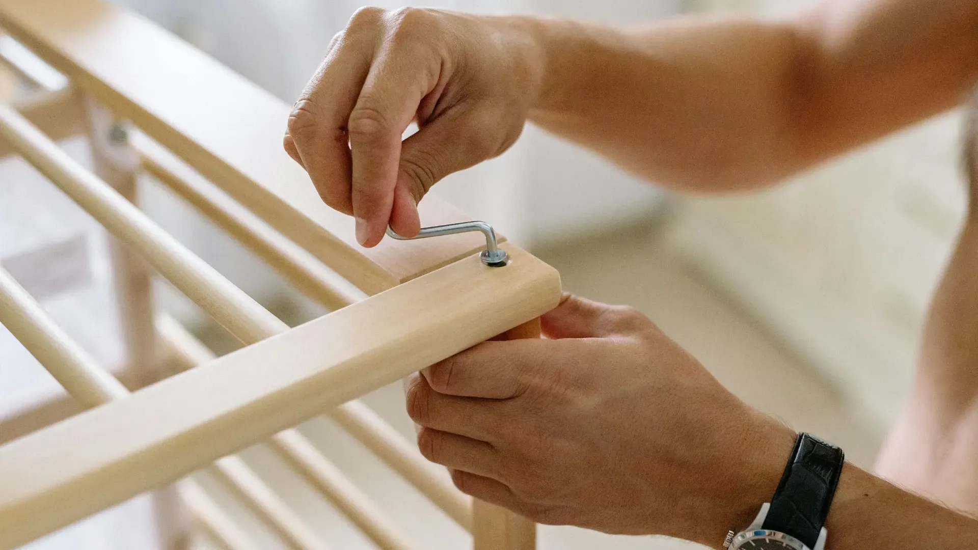 Person attaching hardware to a wooden crib, indoors.