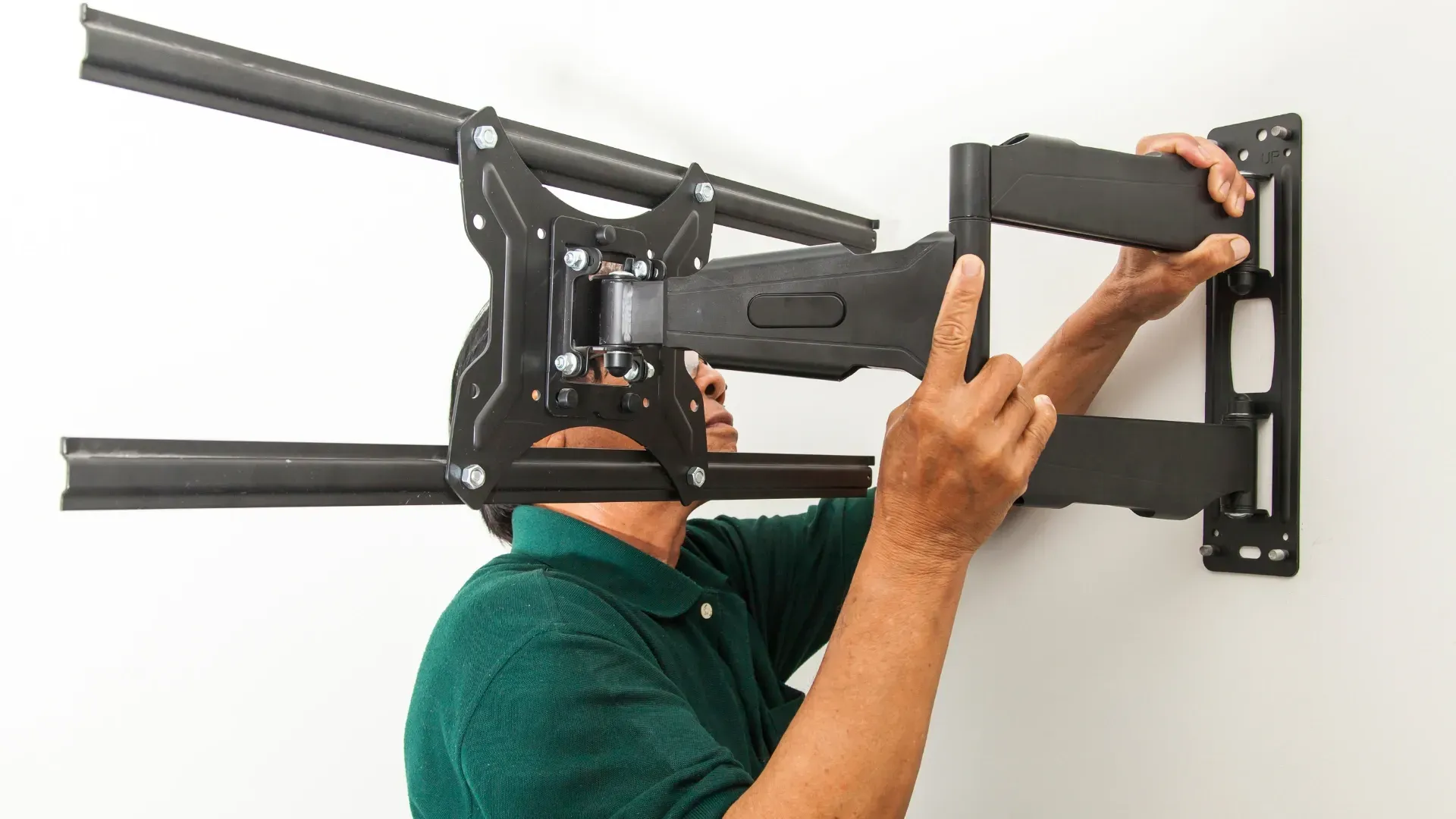 Person mounts black TV bracket on a white wall; arms extended.