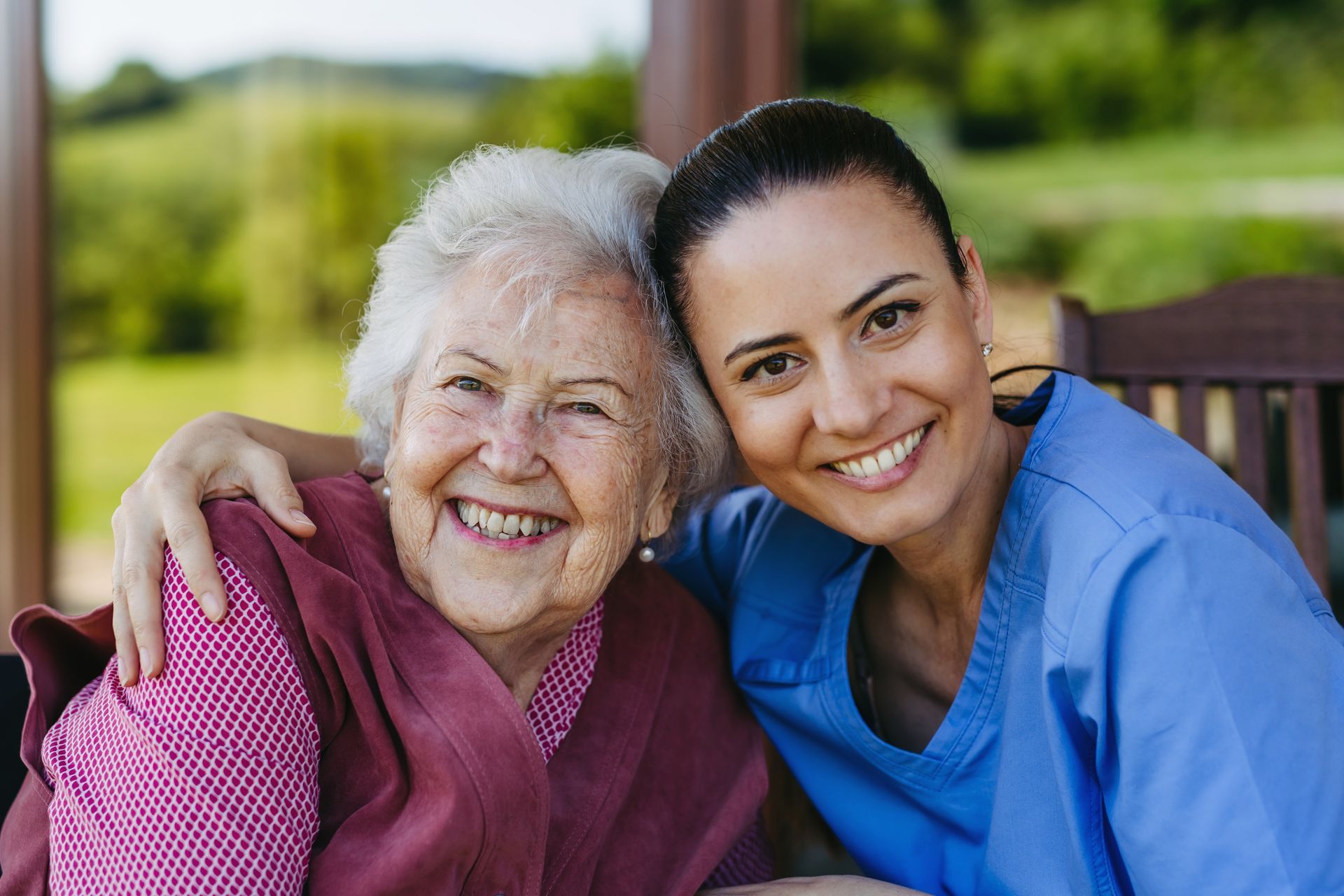 A nurse is hugging an elderly woman on a bench.