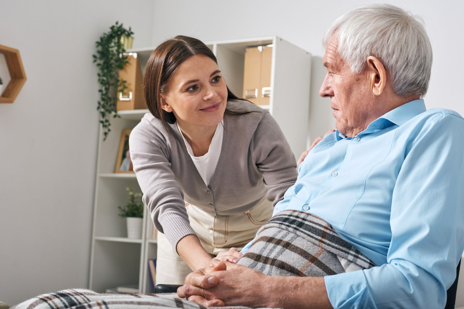 Woman comforts a senior, placing a hand on his shoulder in a well-lit room.