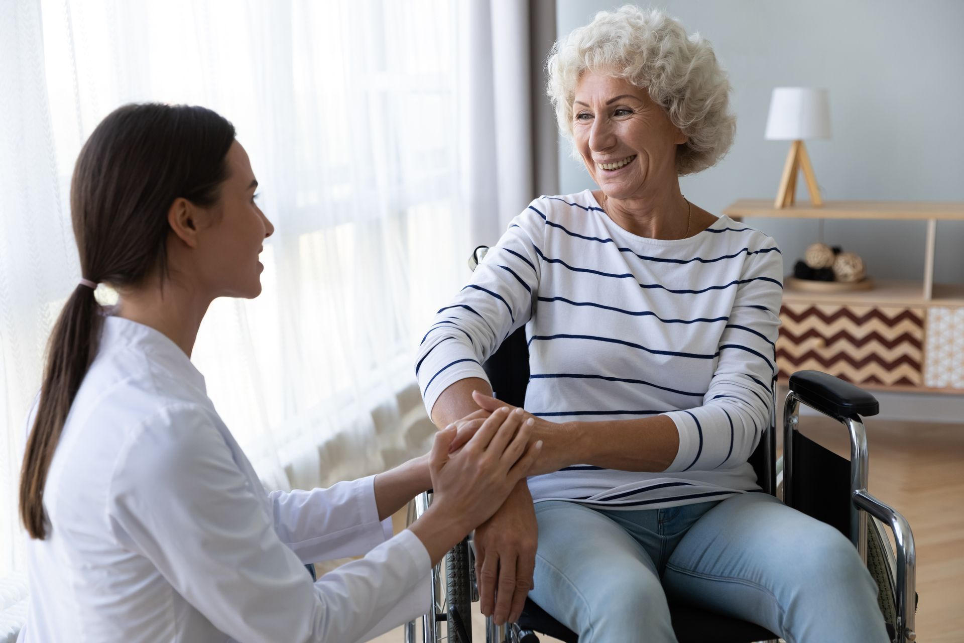 A nurse is holding the hand of an elderly woman in a wheelchair.