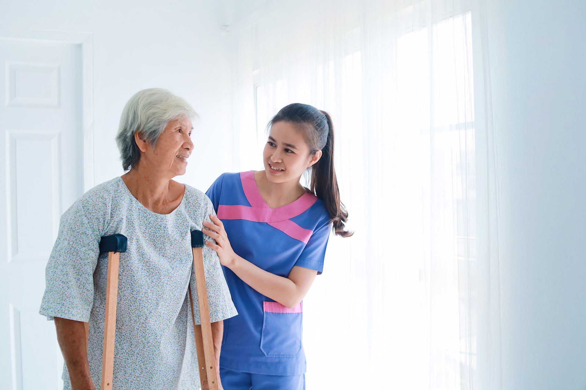 Woman with crutches being assisted by caregiver in bright room.