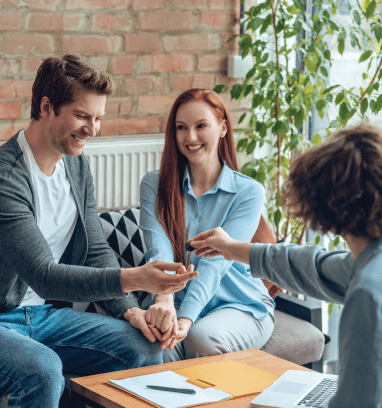 A woman is talking to a man and a woman while sitting at a table with a laptop.