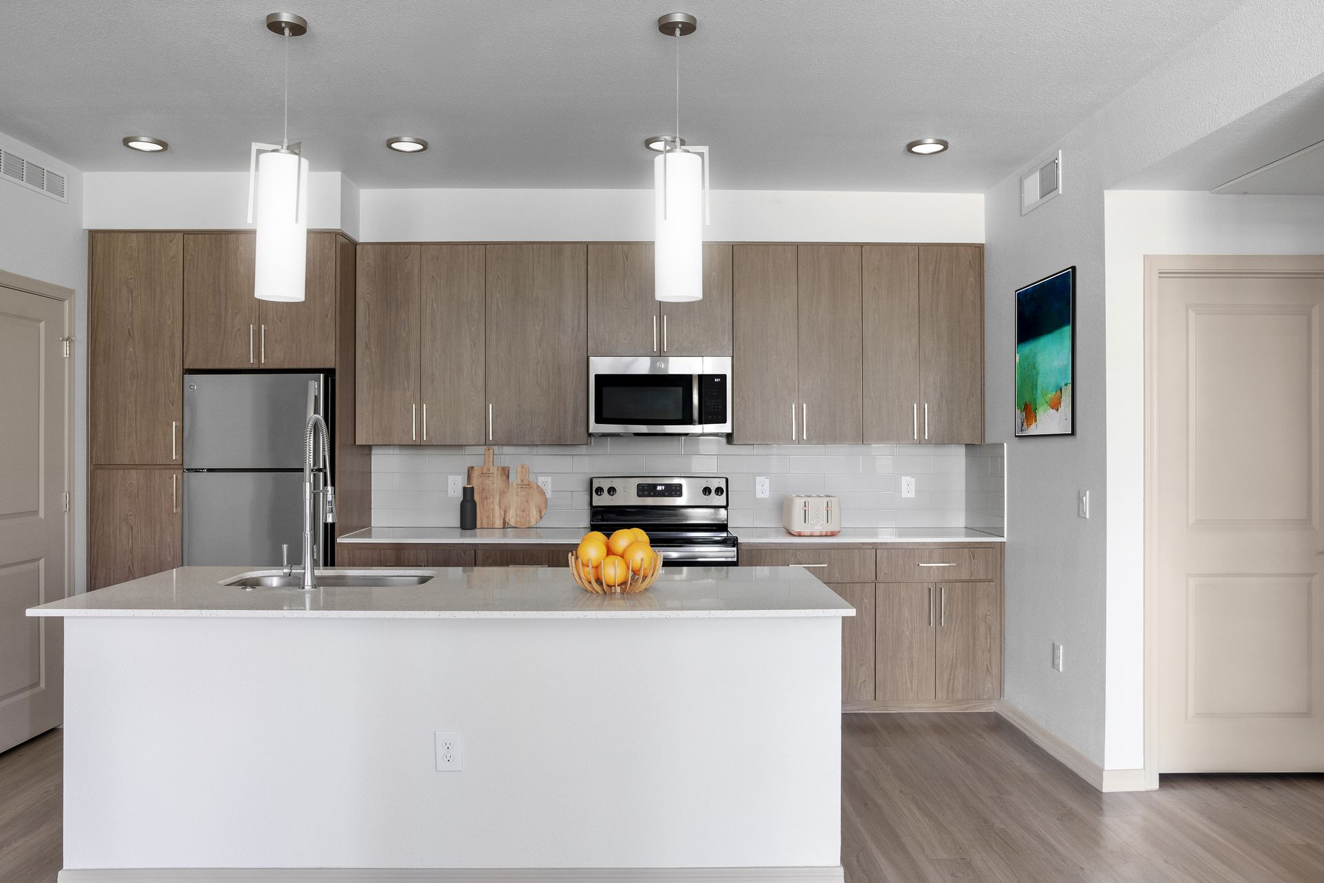 Modern apartment kitchen with island, wood cabinets, stainless steel appliances and a fruit bowl on the island.
