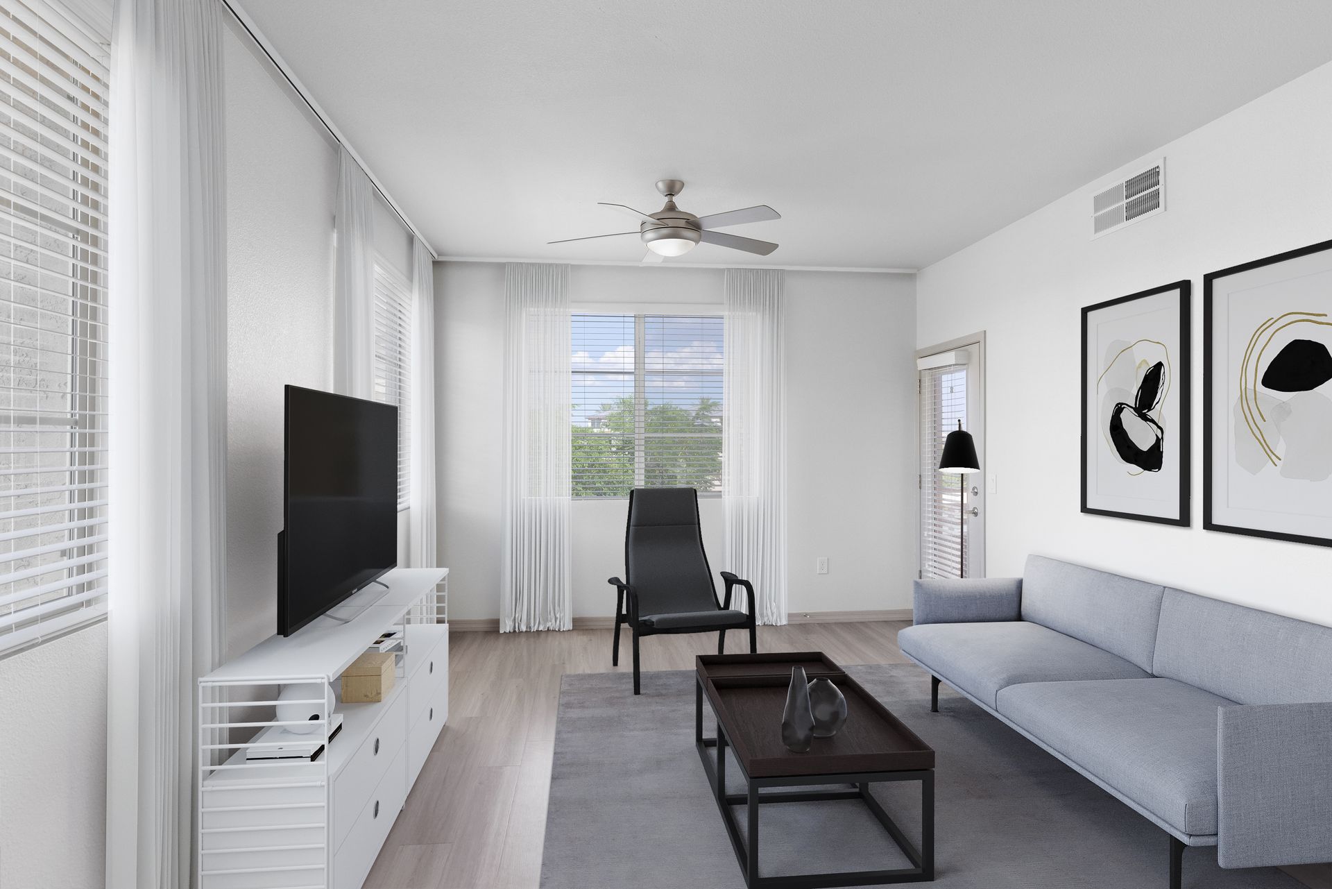 Bright living room with large windows, sheer white curtains, and a gray sofa facing the TV.