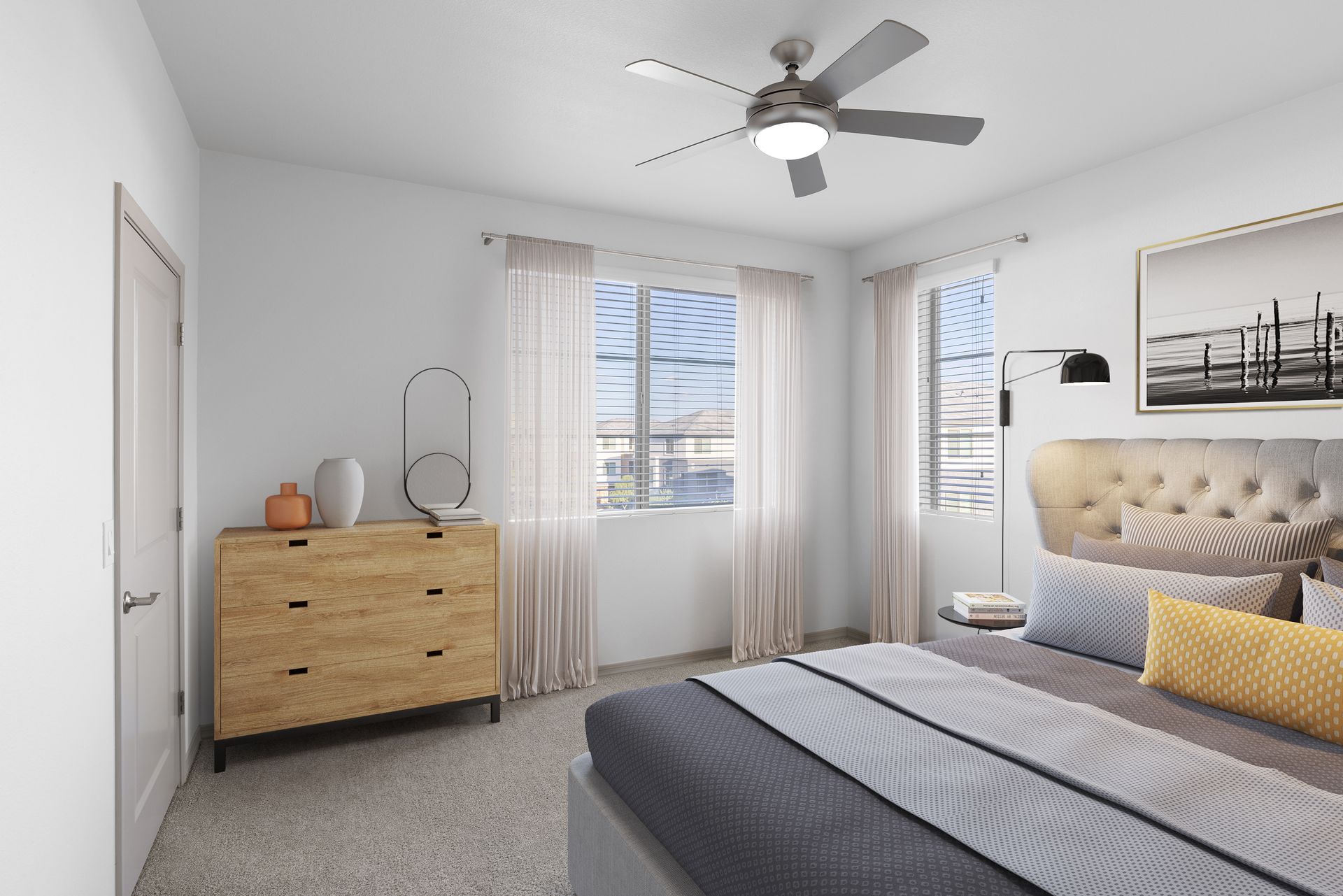 Bright apartment bedroom with a bed, dresser, and large windows with sheer curtains.