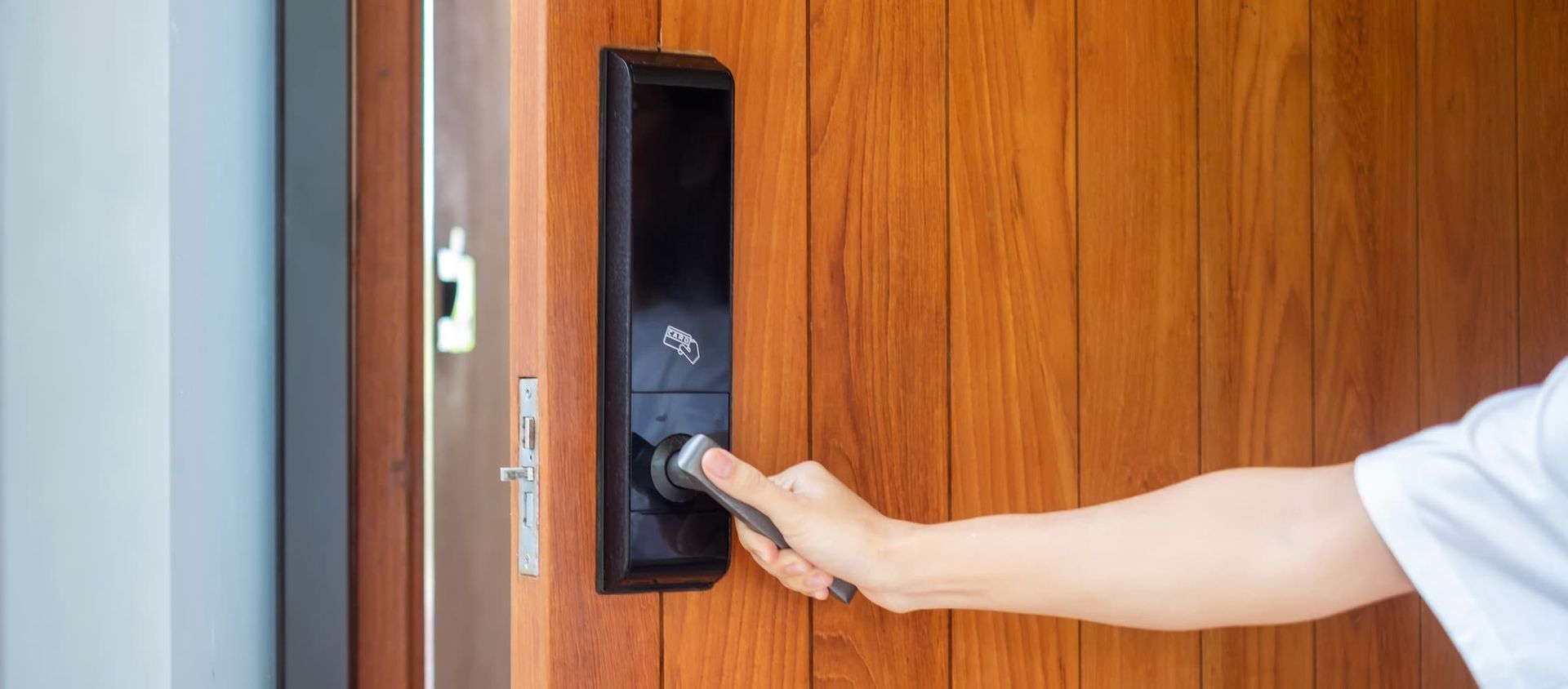 A Person is Opening a Wooden Door With a Smart Door Lock — Coast & Hinterland Mobile Locksmiths In Coolum, QLD
