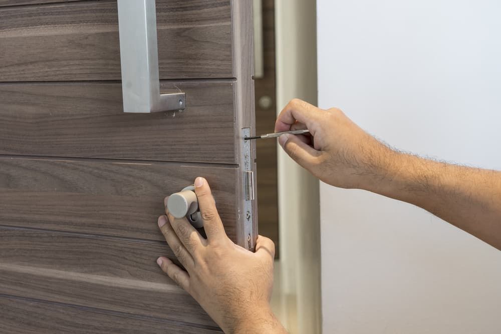 A Person is Fixing a Door With a Screwdriver — Coast & Hinterland Mobile Locksmiths In Tewantin, QLD