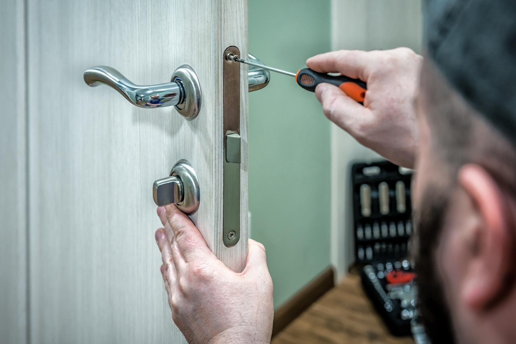 A Man Is Fixing a Wooden Door with A Screwdriver — Coast & Hinterland Mobile Locksmiths In Noosaville, QLD