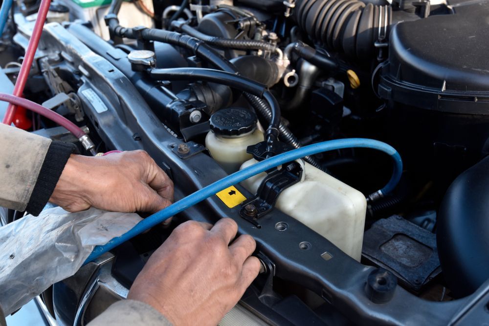 Hands Connecting Blue Hose to Car Engine Bay Components — CE Automotive Service Centre in Garbutt, QLD