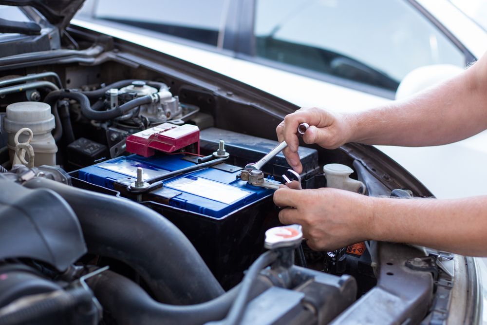 Hands Tightening a Wrench on a Car Battery in an Open Engine Compartment — CE Automotive Service Centre in Garbutt, QLD