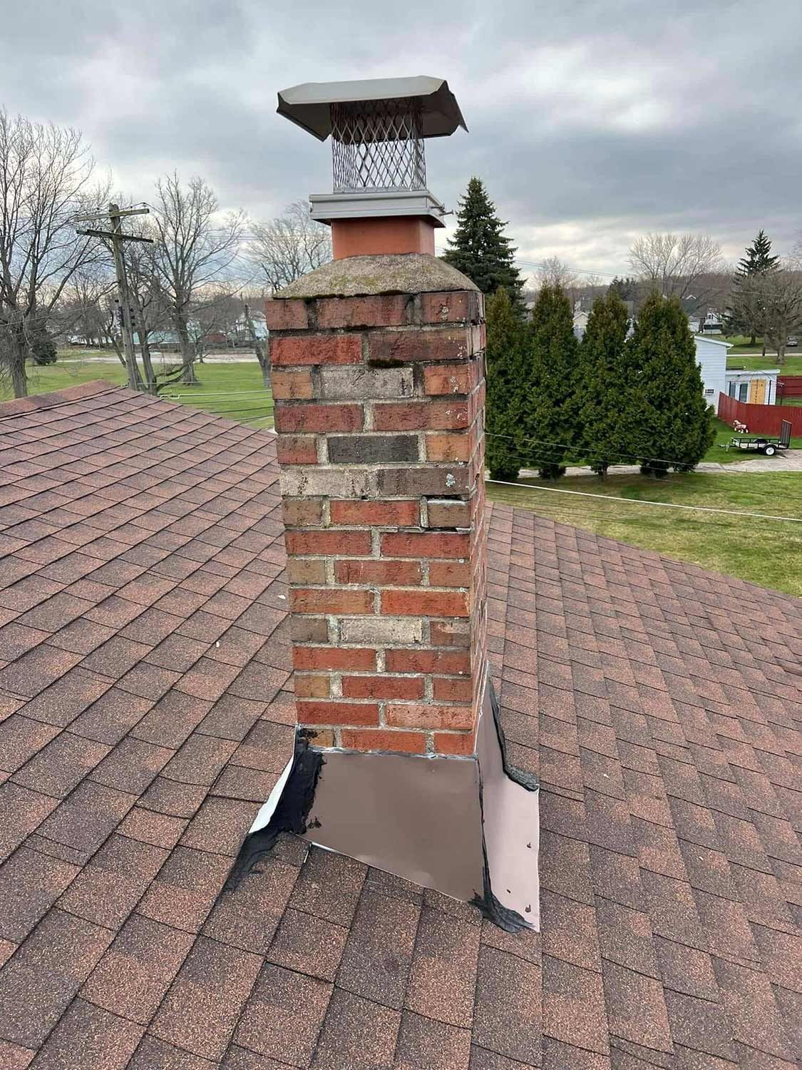 Brick chimney on a shingle roof with a metal cap