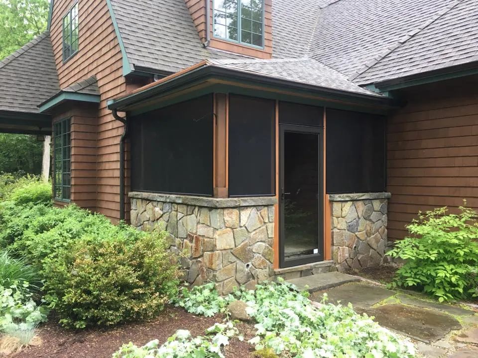 A house with a screened in porch and a stone wall