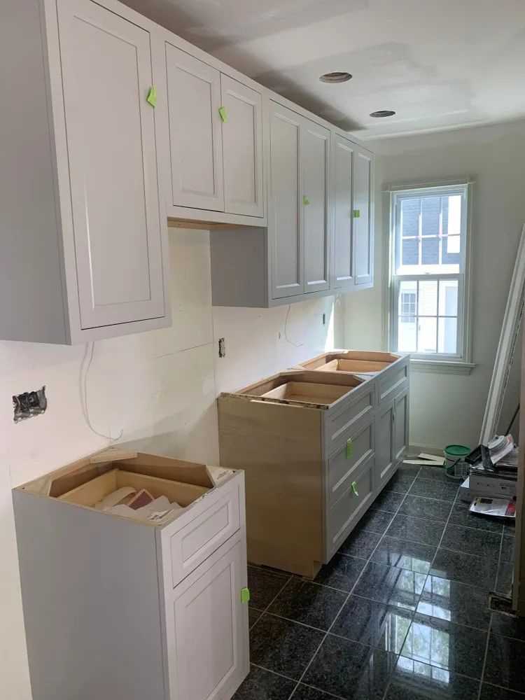 A kitchen under construction with white cabinets and a window.