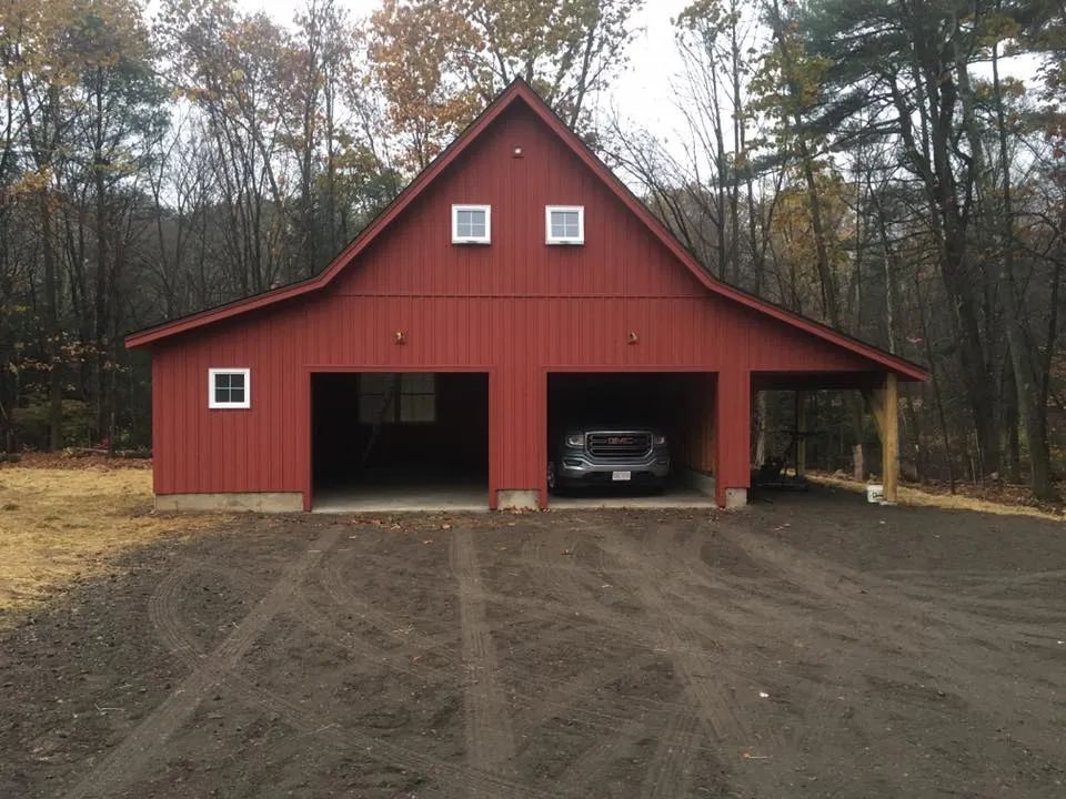 A car is parked in the garage of a red barn