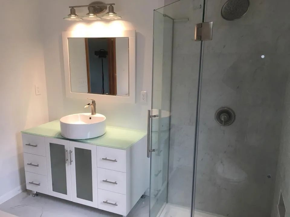 A bathroom with a sink , mirror , and shower stall.