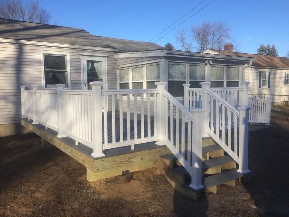 A white house with a deck and stairs in front of it.