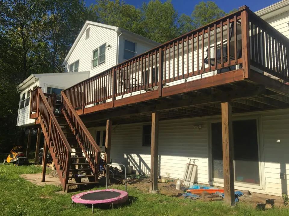 A large wooden deck with stairs and a trampoline in front of a house.
