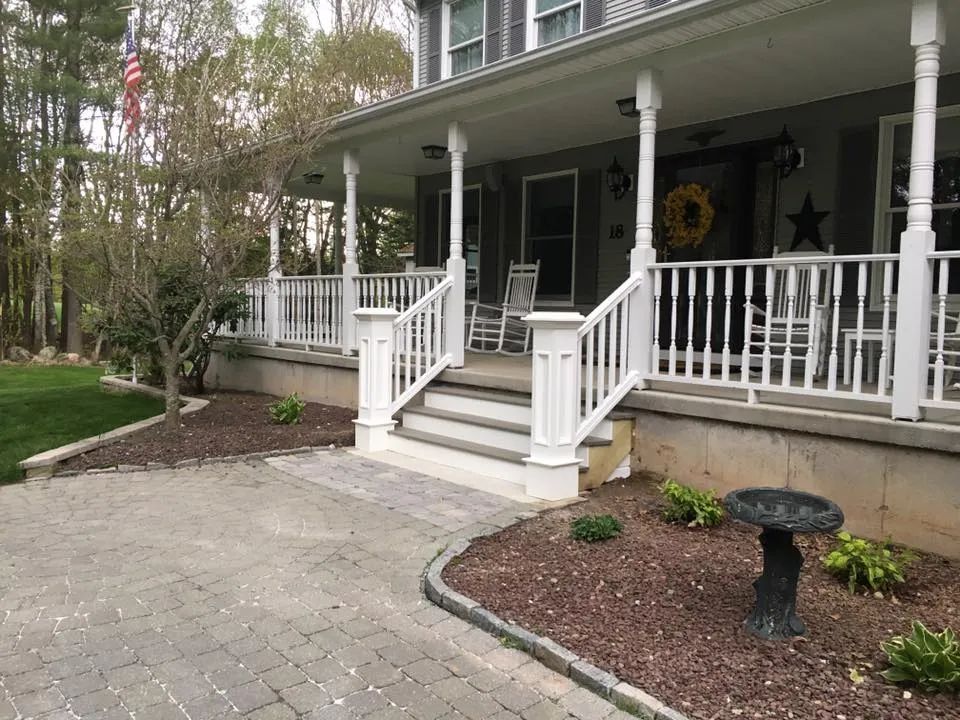 The front porch of a house with a bird bath in front of it.