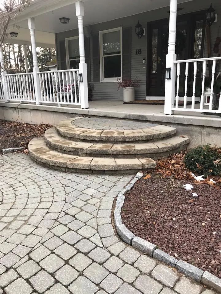 A brick walkway leading to a porch of a house.