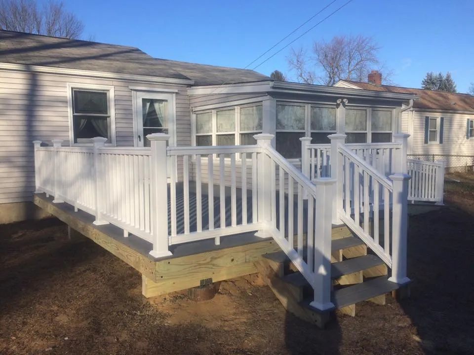 A white house with a deck and stairs in front of it.