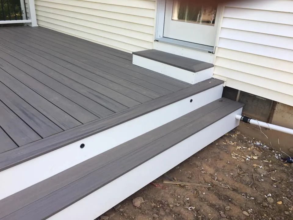 A gray deck with white steps next to a white house.