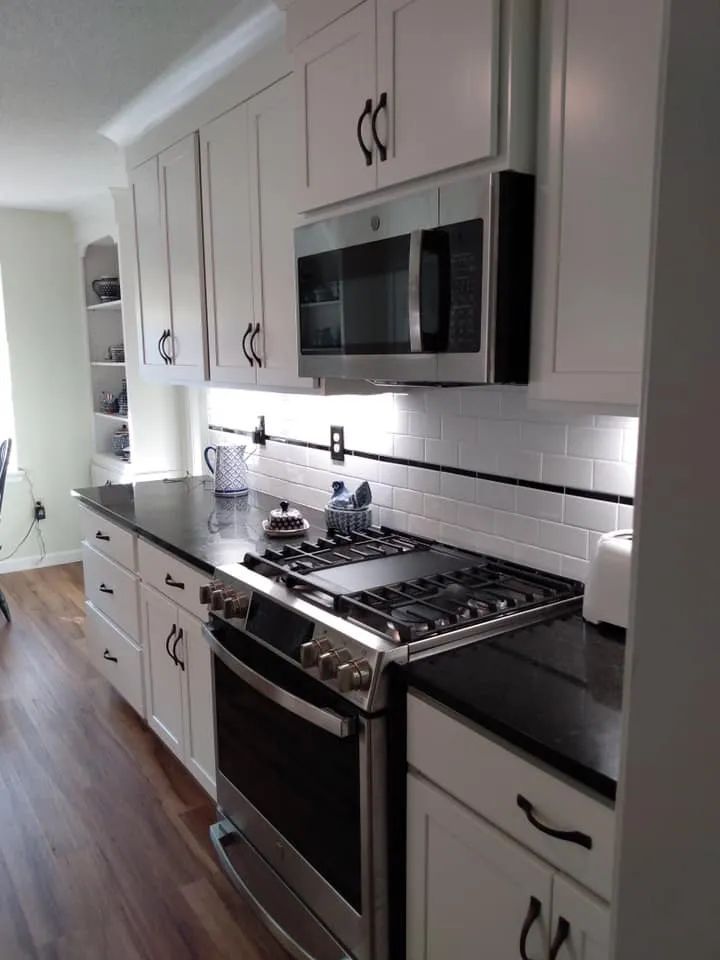 A kitchen with white cabinets , a stove , a microwave , and a black counter top.
