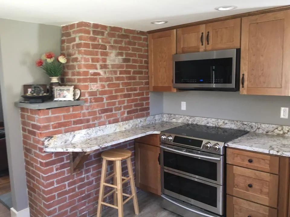 A kitchen with wooden cabinets , a stove , a microwave and a brick wall.
