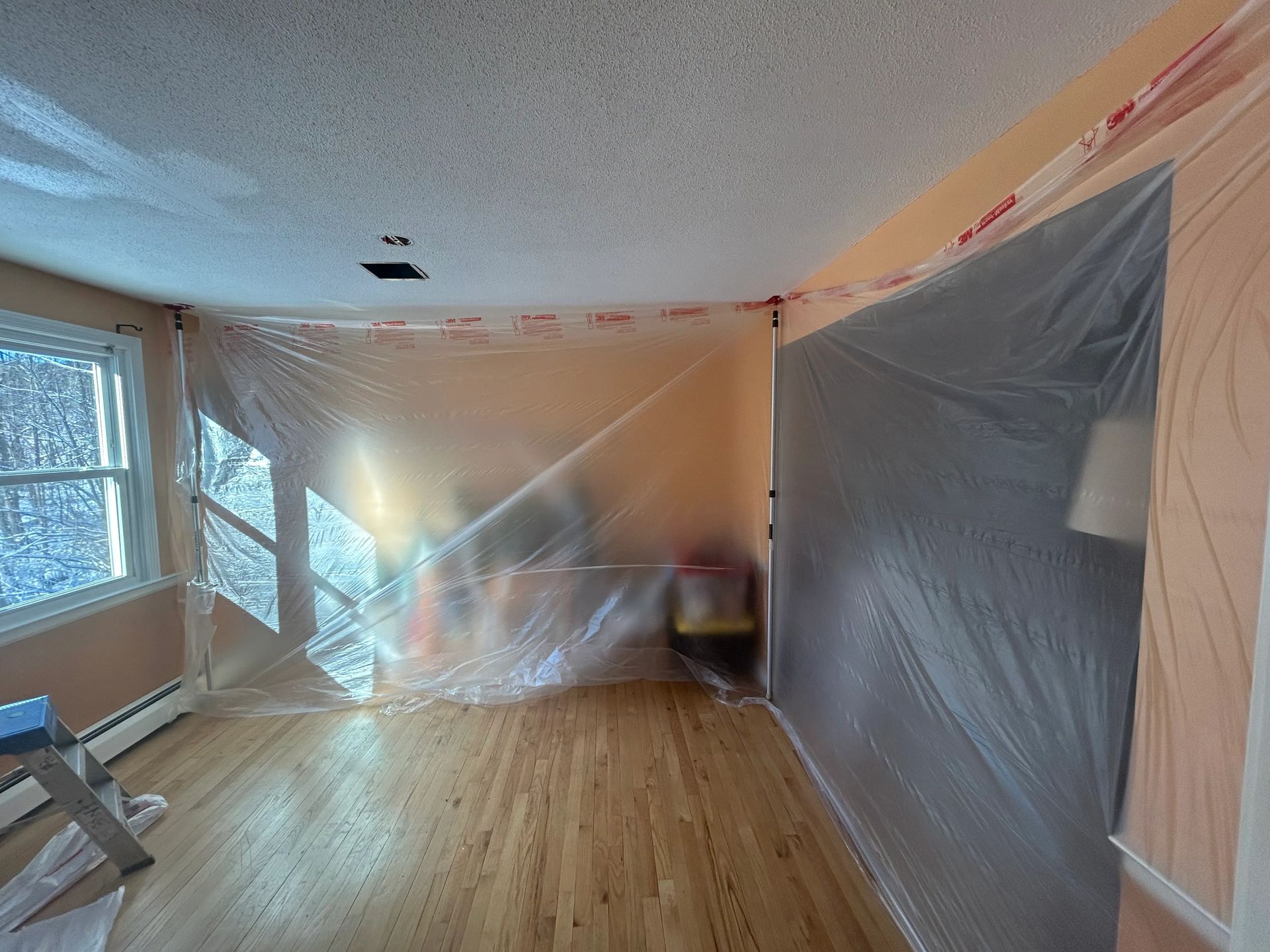 A living room is covered in plastic while being painted.