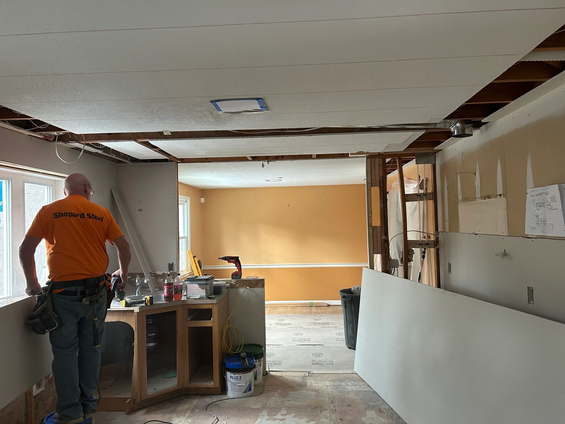 A man in an orange shirt is standing in a room under construction.