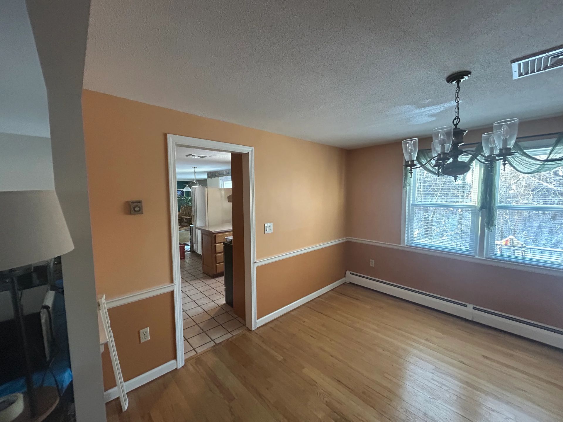 An empty dining room with hardwood floors and a chandelier hanging from the ceiling.