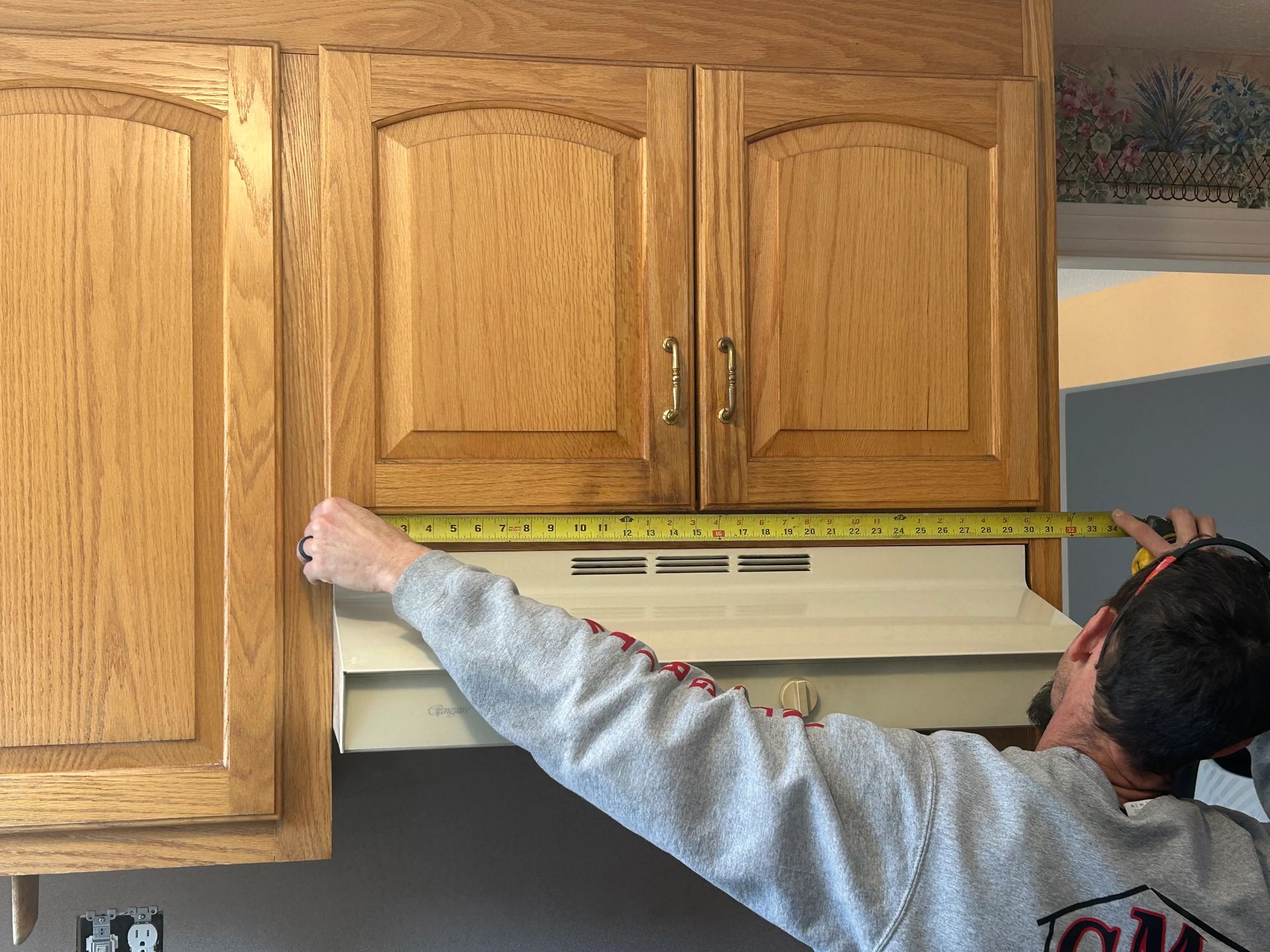 A man is measuring a cabinet with a tape measure.