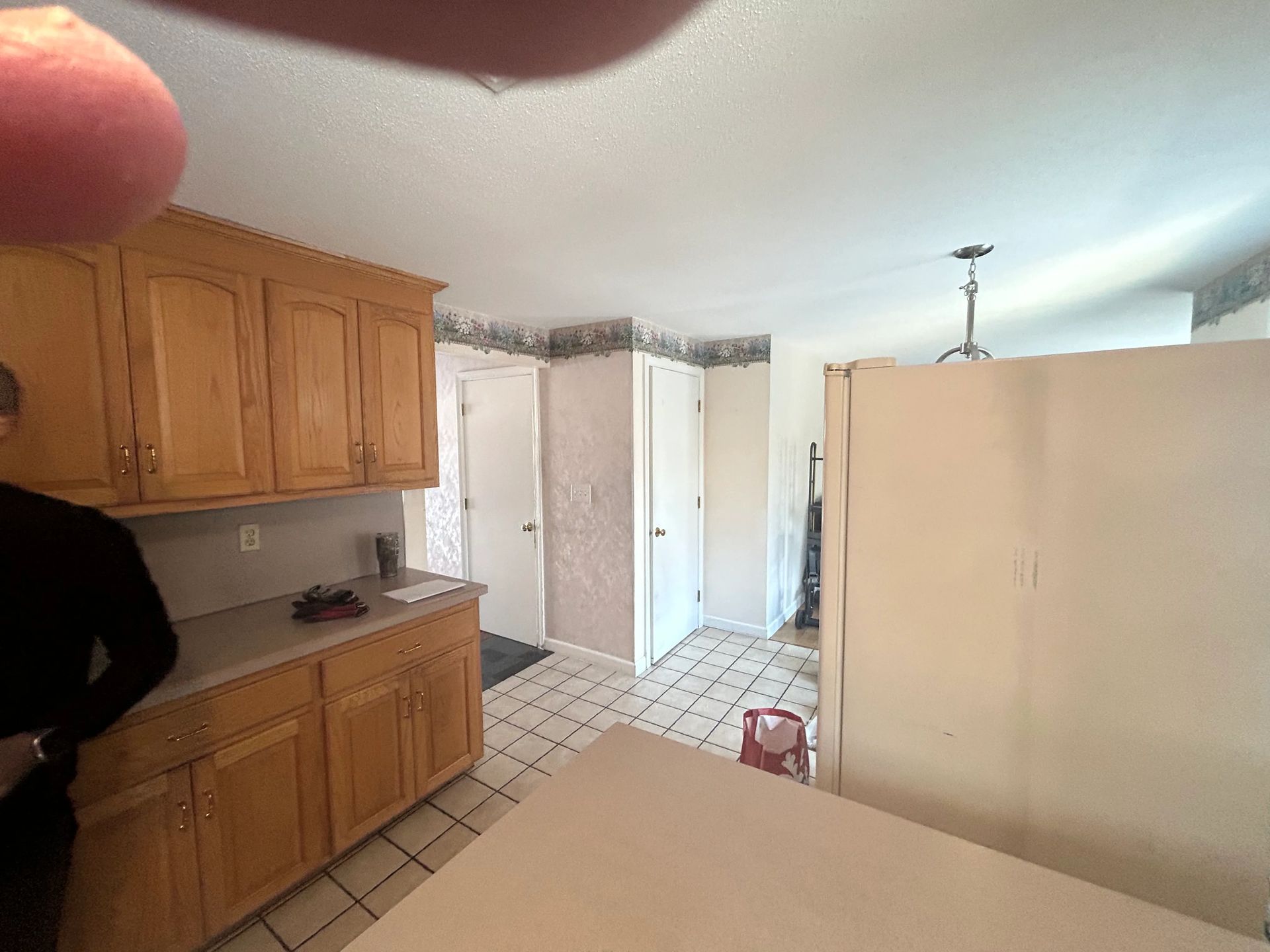 A person is standing in a kitchen with wooden cabinets and a refrigerator.