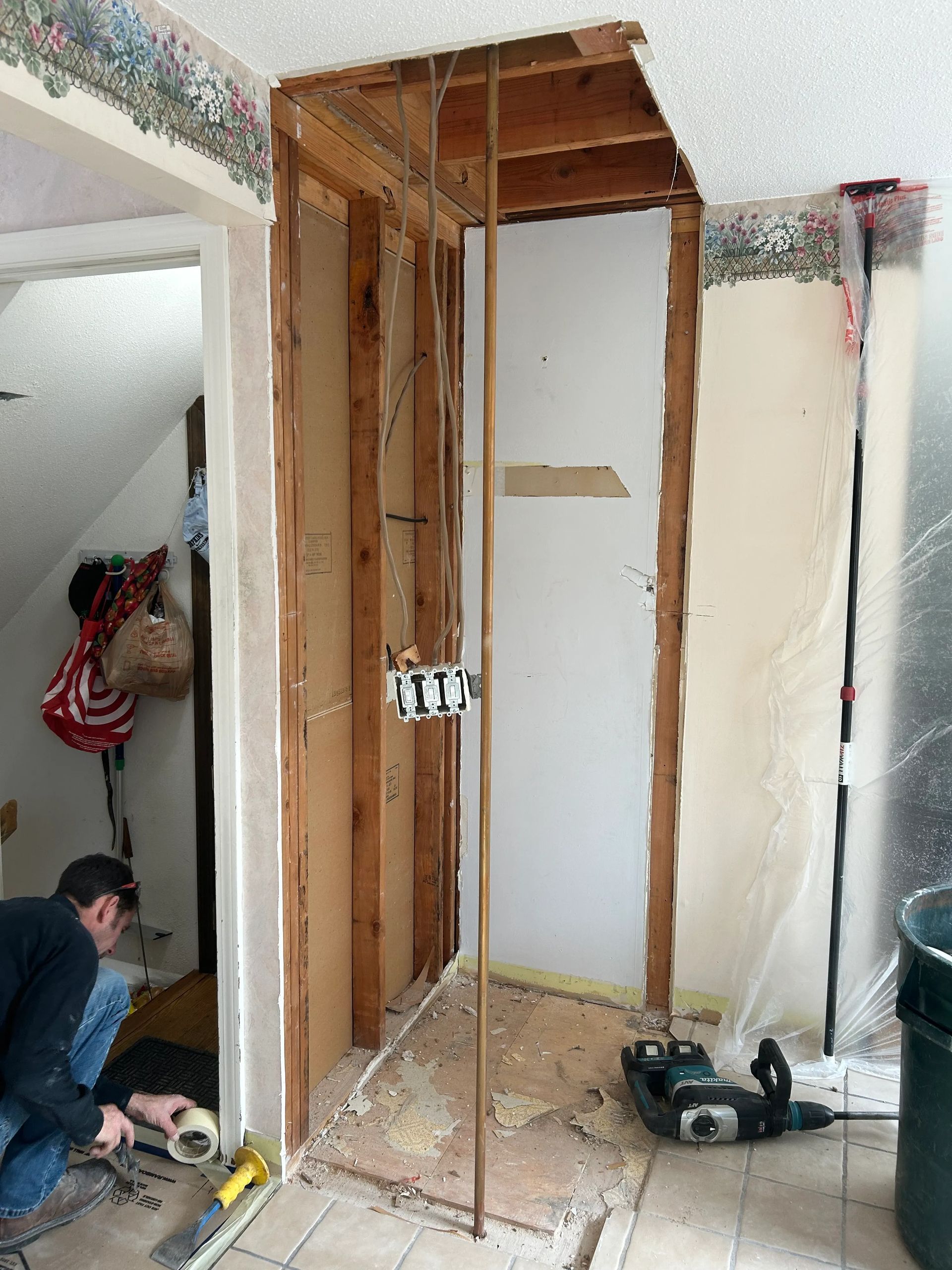 A man is kneeling on the floor in a room with a hole in the ceiling.