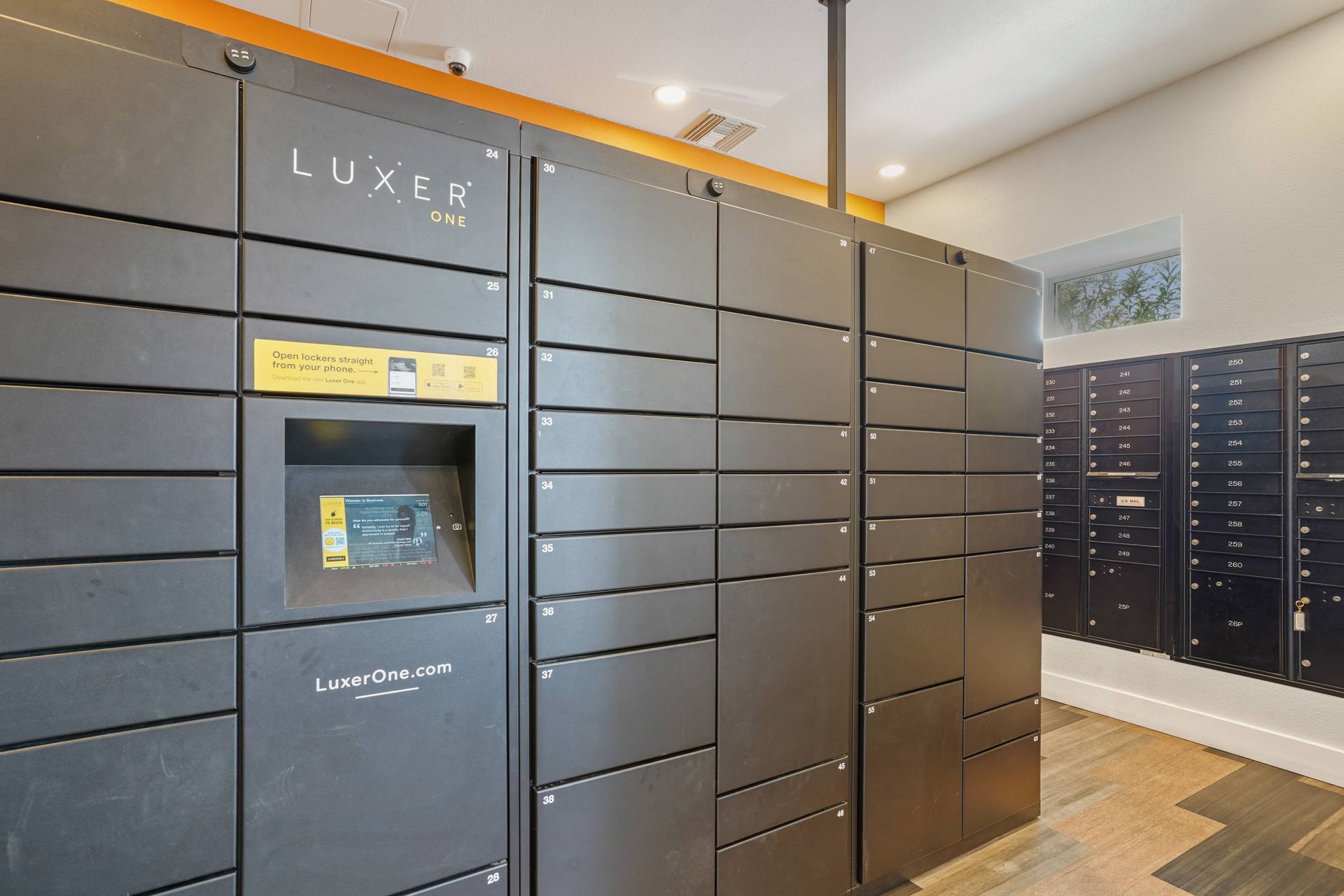Interior view of a large row of gray parcel lockers in a building lobby.