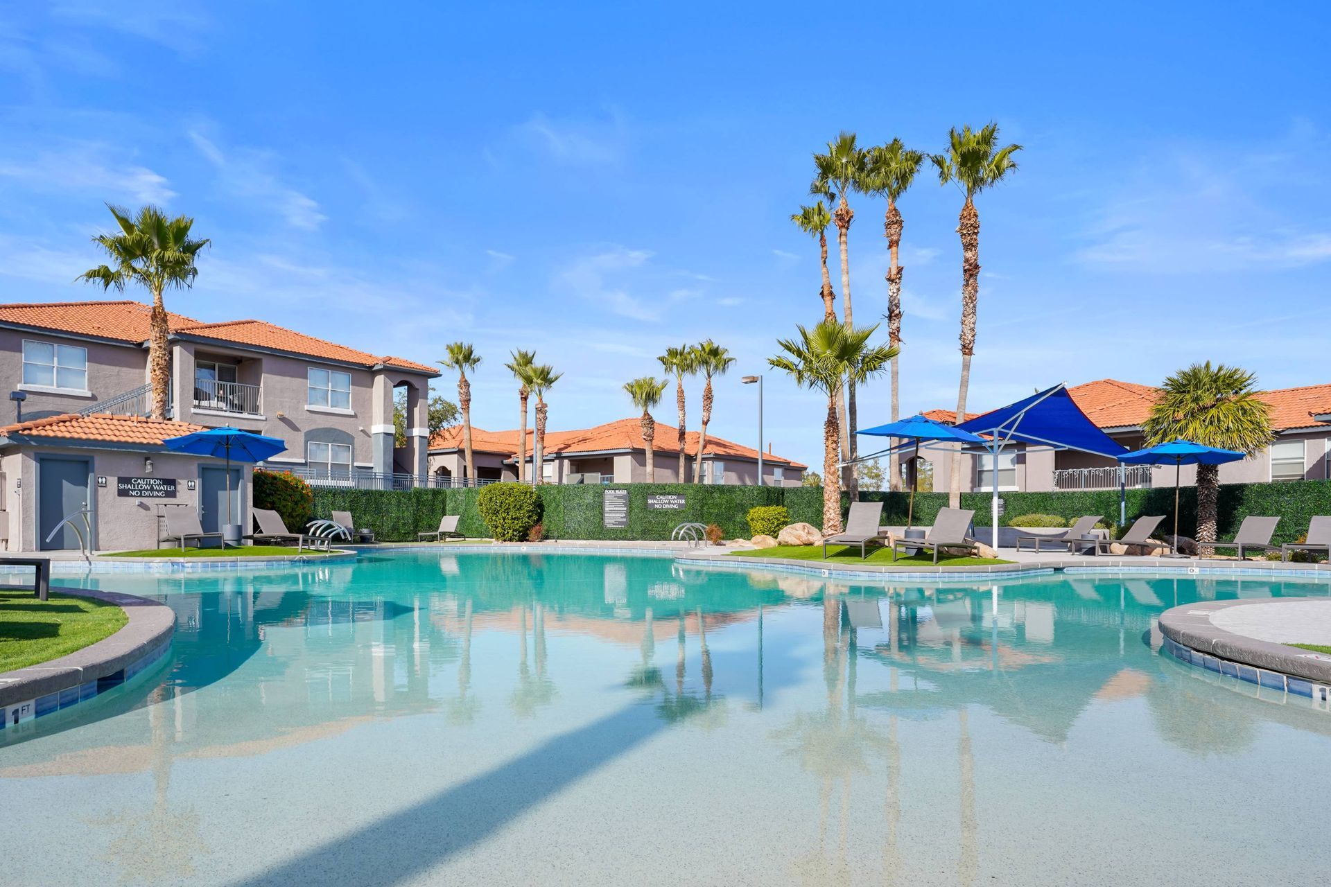 Outdoor apartment community pool with palm trees, lounge chairs, and blue shade umbrellas.
