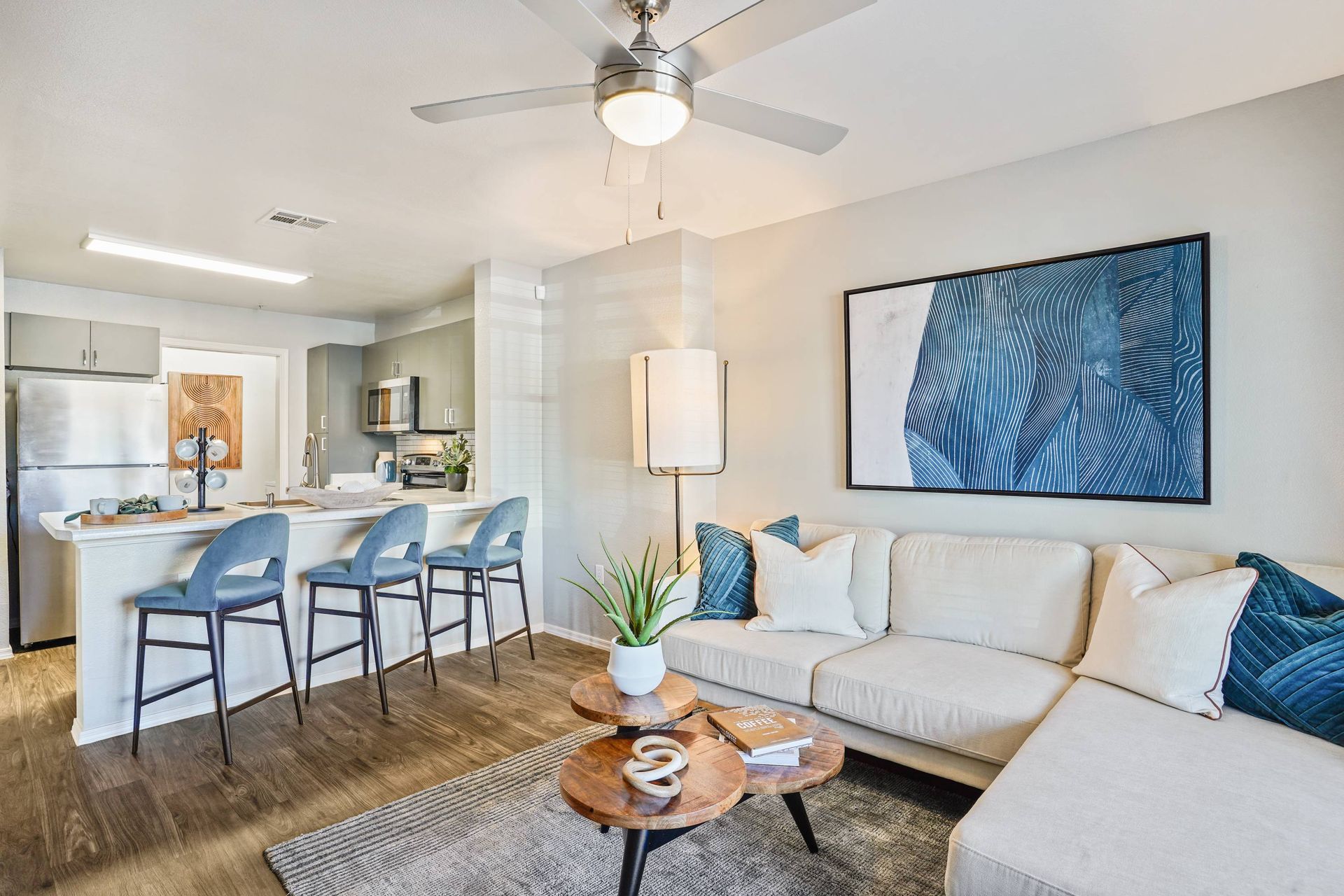 Open-concept living area with kitchen island, blue bar stools, and a light sofa.