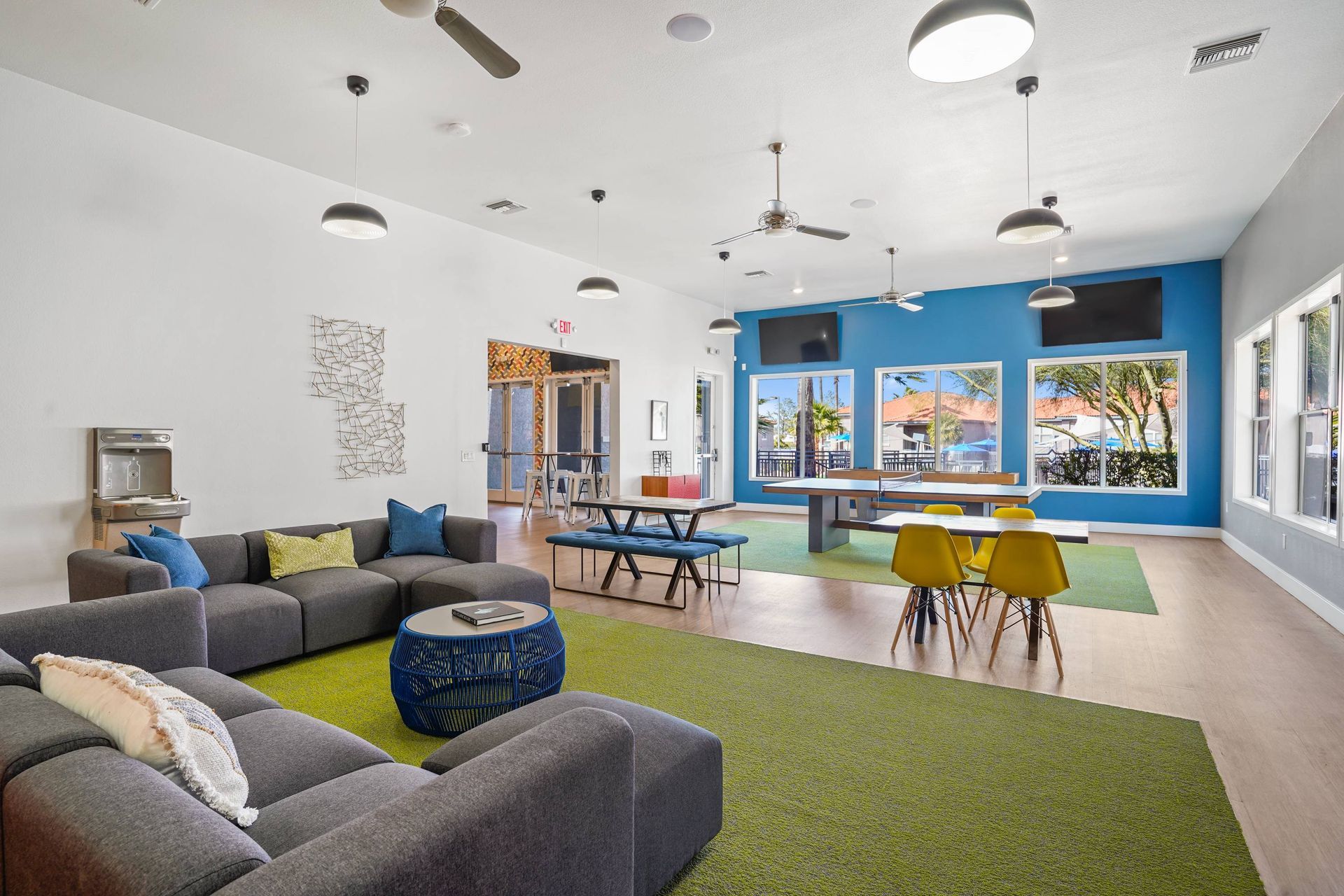 Interior community lounge with gray sectional sofas, colorful accents, tables, and large windows.