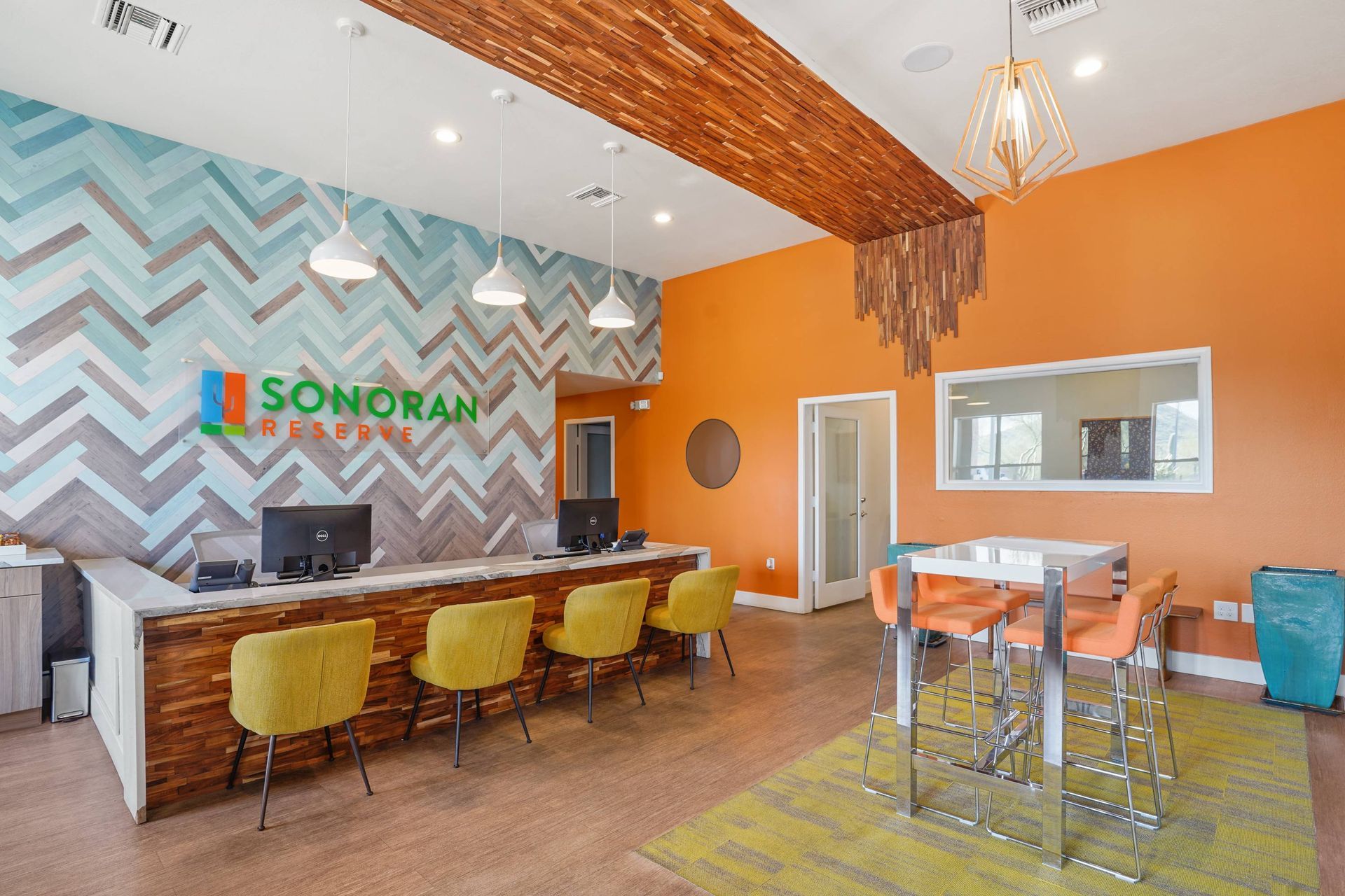 Leasing lobby with a long reception desk, chevron wall design, and orange accents.