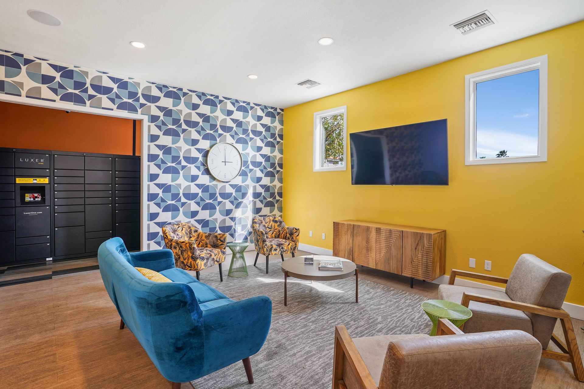 Modern communal lounge with blue geometric wallpaper, a yellow accent wall, and a wall-mounted TV.