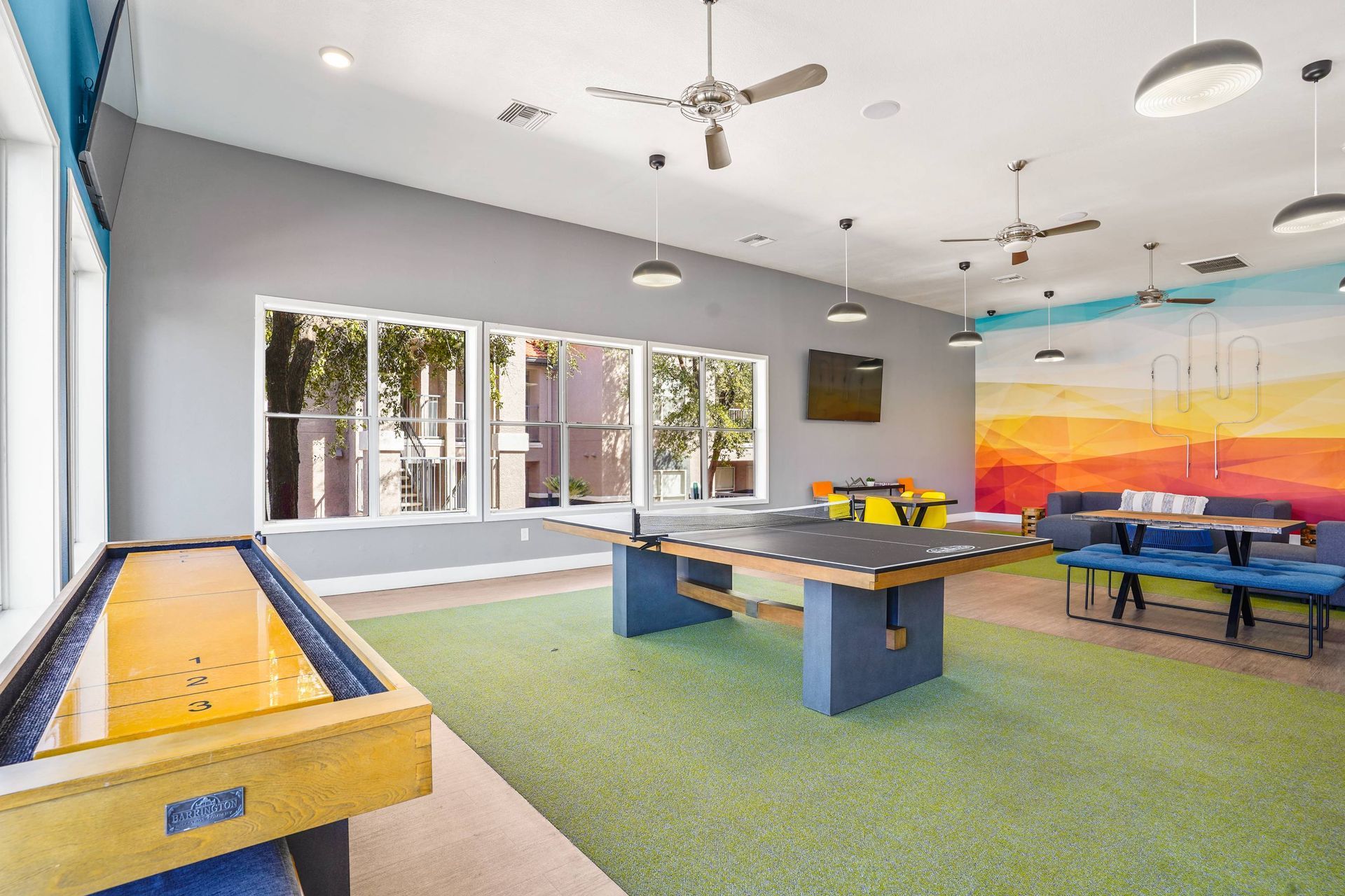 Bright indoor community lounge featuring a ping-pong table, seating, and a colorful mural.