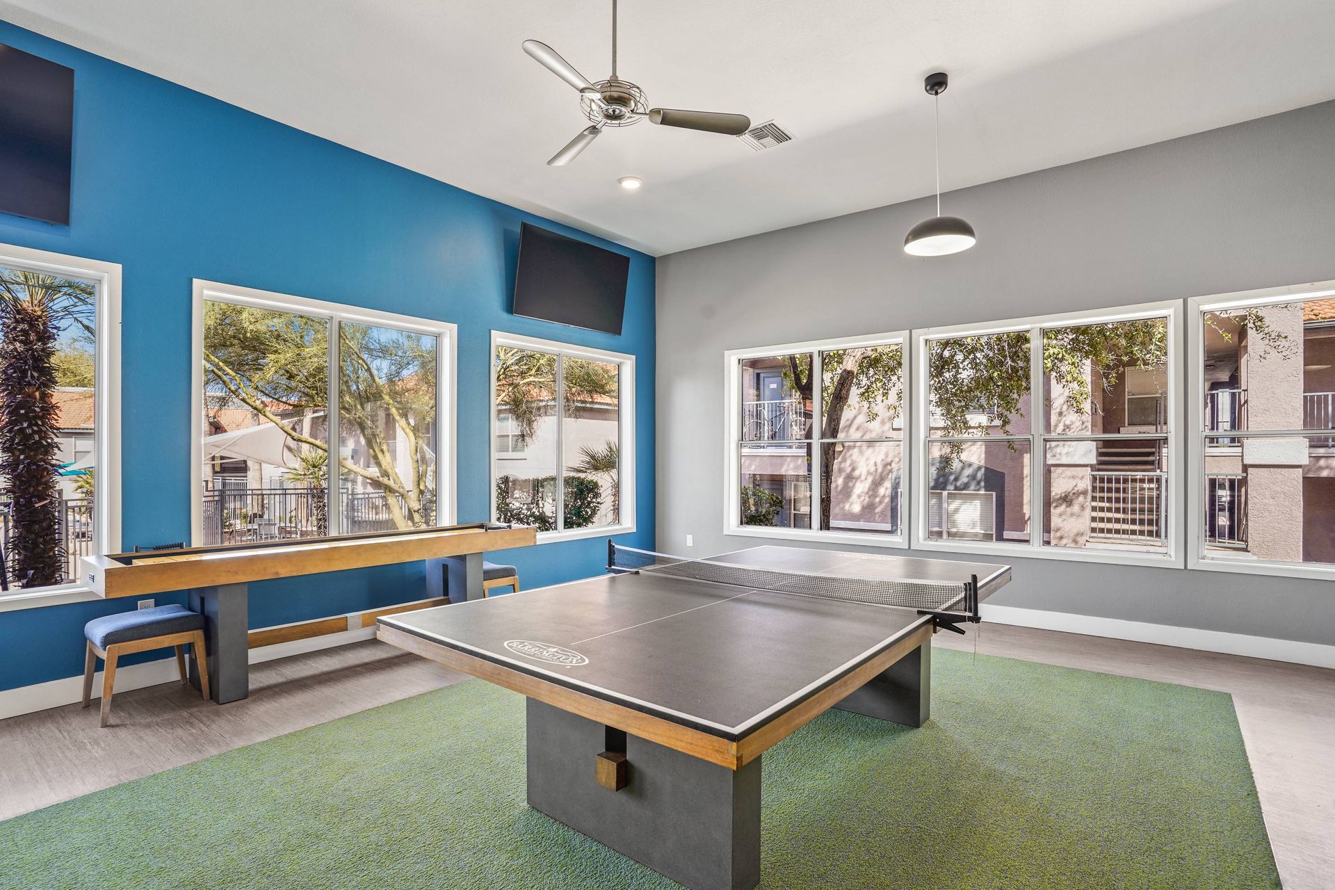 Indoor community recreation room with a ping-pong table, bench seating, and large windows.