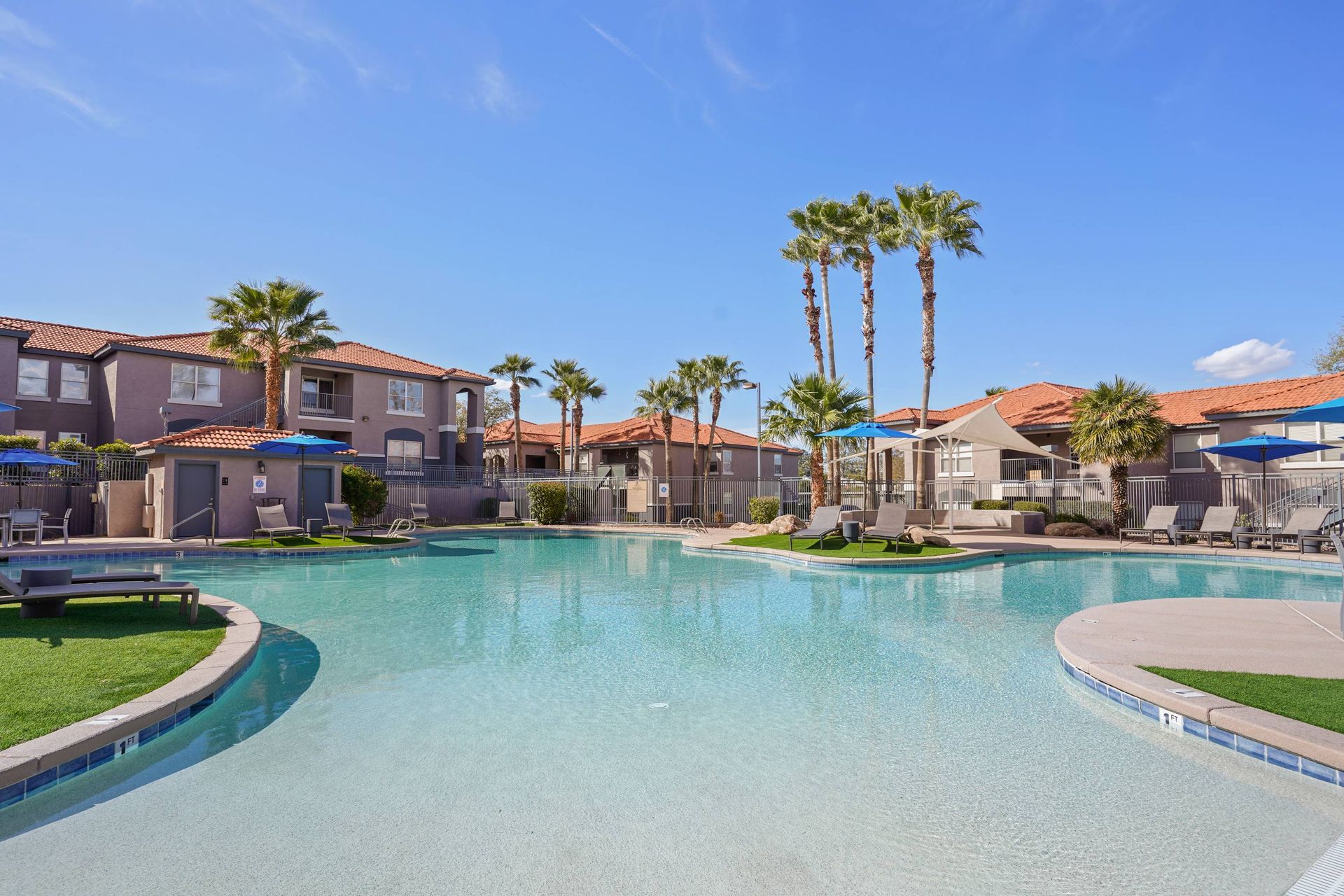 Outdoor apartment community pool with palm trees, lounge chairs, and umbrellas.